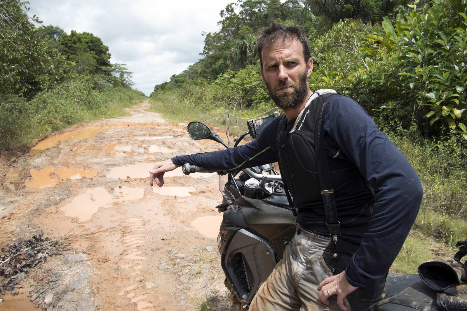Ryan Pyle beside his motorcycle on a muddy road in Brazil